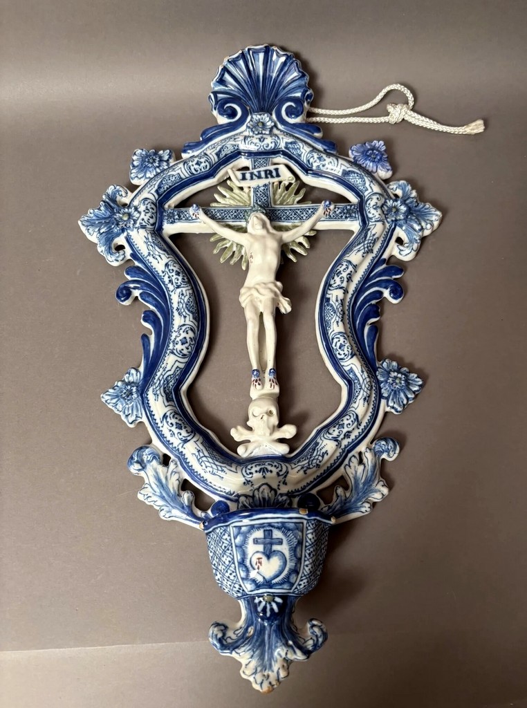 Marseille Bénitier en faïence formé du Christ en croix dans un encadrement à décor en camaïeu bleu de rinceaux feuillagés surmonté d'une coquille