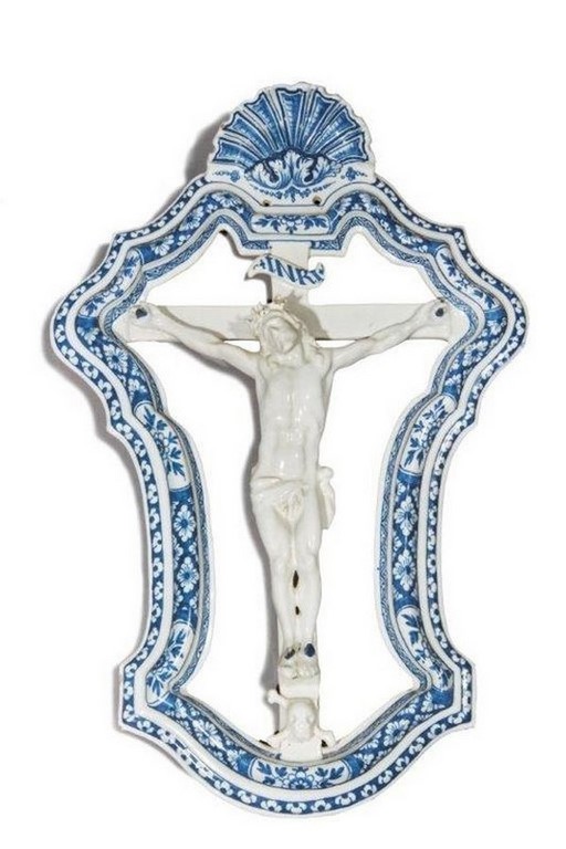 MARSEILLE. Christ en croix en faïence dans un cadre rocaille, sans fond, à décor floral, sommé d’une coquille, en camaïeu bleu.