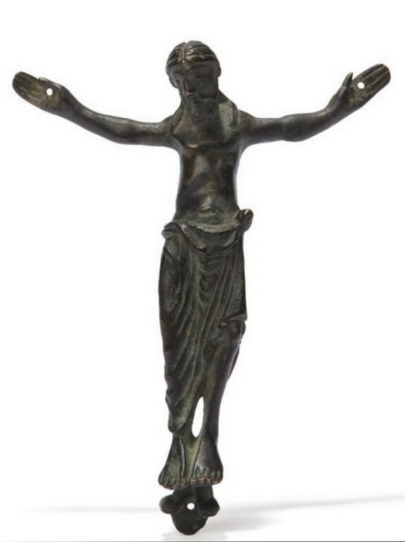 Christ en bronze patiné. Le dos creux, il est représenté vivant, les yeux en relief, les cheveux séparés par une raie médiane retombant sur les épaules, les bras écartés terminés par de larges mains, les jambes parallèles presque entièrement recouvertes par un important perizonium aux amples plis.