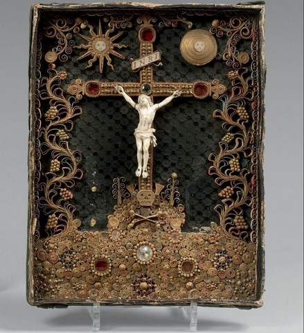 oîte cadre contenant un Christ en ivoire, le périzonium noué. Croix, terrasse et encadrements de paperolles dorées et polychrome enchassant des cabochons teintés.